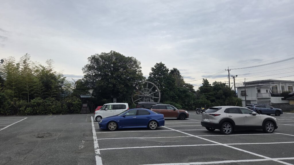 Exterior view of Koshu Hoto Kosaku Ryuo Tamagawa branch featuring a traditional waterwheel and spacious parking lot